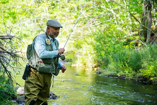 A mature fisherman fly-fishing on a trout stream in afternoon light.