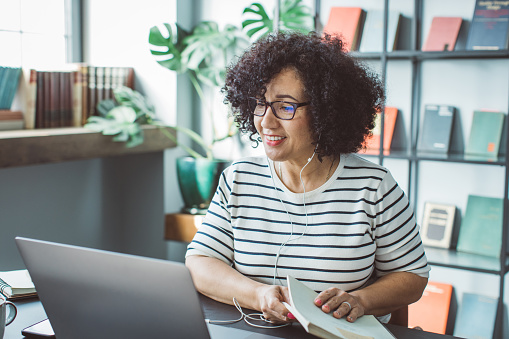 Mature woman at her office. She is book publisher and having video call on laptop with author.