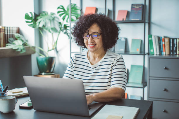 Book publisher at office Mature woman at her office. She is book publisher and reading book script or writing mail on laptop. publisher photos stock pictures, royalty-free photos & images
