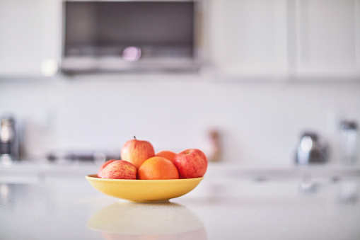 Assorted fruit in a yellow bowl on an island in a bright white modern kitchen
