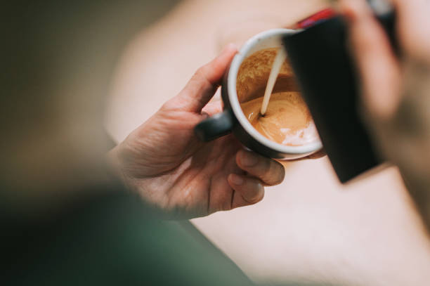 sopra la spalla asiatico cinese barista maschio versando latte schiuma sulla tazza di caffè preparato caffè latte art al bancone del bar - pouring coffee human hand cup foto e immagini stock