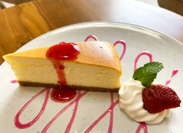 beautiful cheesecake presentation in the restaurant, with cream fla, red strawberry jam and fresh strawberry fruit as the garnish