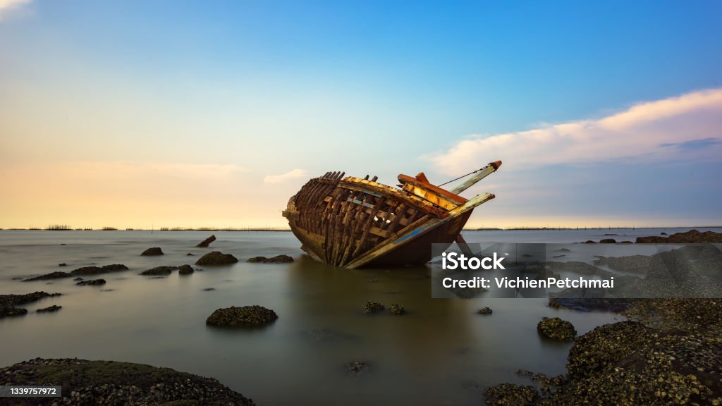 Boat deteriorate breaking down laying in the coast side with sunset in background Electric Plug Stock Photo