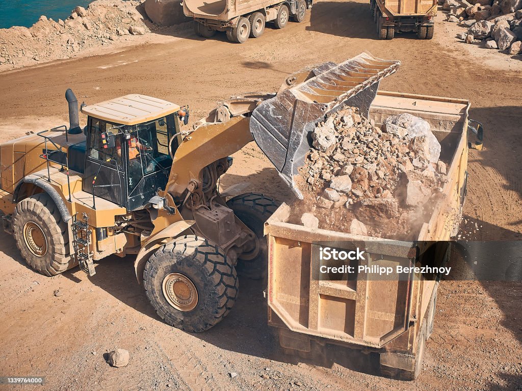 Wheel loader loads tipper with soil Front wheel loader loads dump truck with crushed stone. Earthmoving works at construction site. Transportation of construction materials Loading Stock Photo