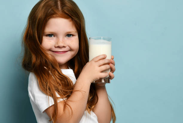 urocza rudowłosa dziewczynka dziecko pijące mleko lub jogurt kefirowy radośnie uśmiechając się na jasnoniebieskim tle. koncepcja zdrowia i diety - glasses child red hair little girls zdjęcia i obrazy z banku zdjęć
