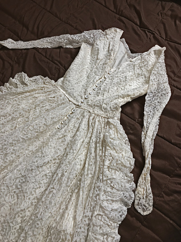 A wedding dress from 1961 draped on a bed with a dark comforter.