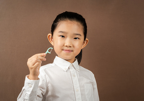 Little Girl Holding Dental Floss Stick on Brown Background