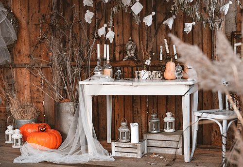 Halloween decorated yard of old wooden house, vintage white table with candles and pumpkins