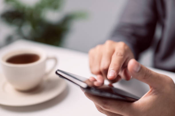 istock Male hands touching mobile phone. Man using smartphone while sitting at the white table his modern home. 1339786258