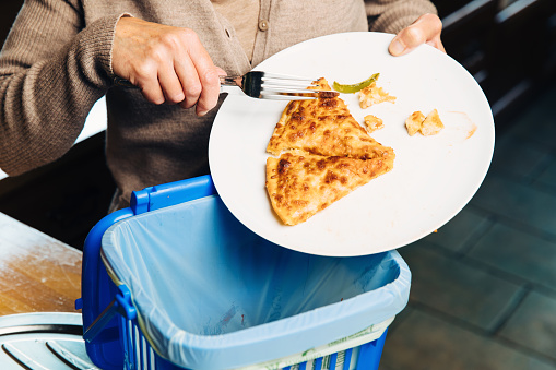 Woman scraping pizza leftovers into a food waste bin. The bin contains a degradeable plastic bag which is knotted closed and put in a special community container for recycling.