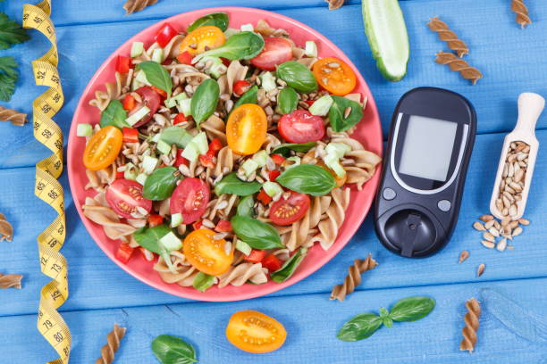 Glucose meter for checking sugar level and fresh salad with wholegrain pasta and vegetables. Best food for diabetics stock photo