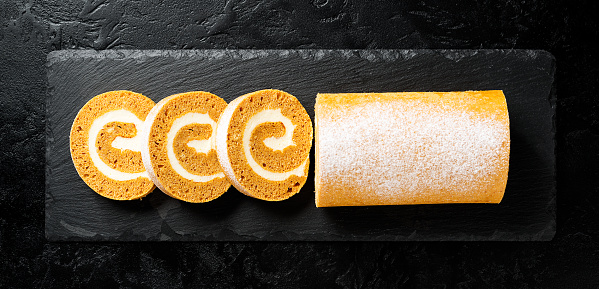 Pumpkin Cake Roll with Cream Cheese Filling. Autumn Baking. Black background, top view