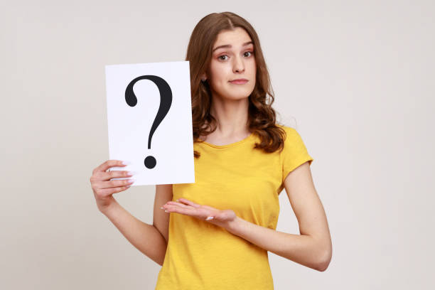 young attractive brown haired young woman in yellow casual style t-shirt holding paper with question mark, making decision, solving problem. - pensive question mark teenager adversity imagens e fotografias de stock