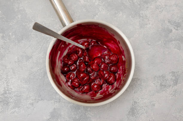 istock Cherry cooked with sugar and starch in a saucepan to make chocolate roll cake Black forest on a gray concrete background. Recipe step by step. Top view. 1339797315
