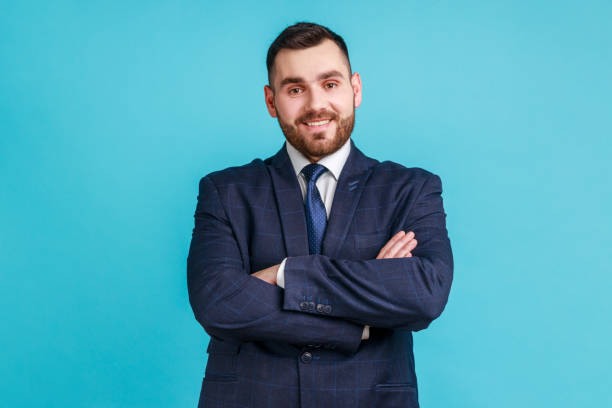 young adult attractive businessman wearing official style suit posing with happy confident expression, looking at camera, keeping arms folded. - forward fold imagens e fotografias de stock