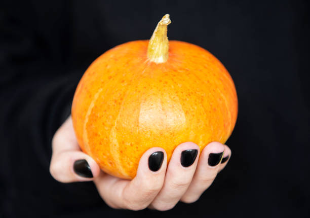 istock Female hands holding funny pumpkins on black background 1339800330