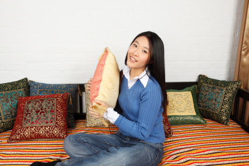 A cheerful woman holding pillow and smiling at viewer.