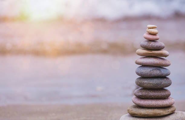 istock Rock balancing or stone stacking, rock stone or sea pebbles pile or pyramid on sand symbolizing zen, harmony, balance. Ocean water and sunset on background. Relaxation concept. Empty space for text. 1339805097