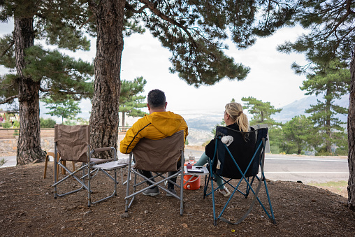 Rear view of mature couple sitting chair in mountain camp.