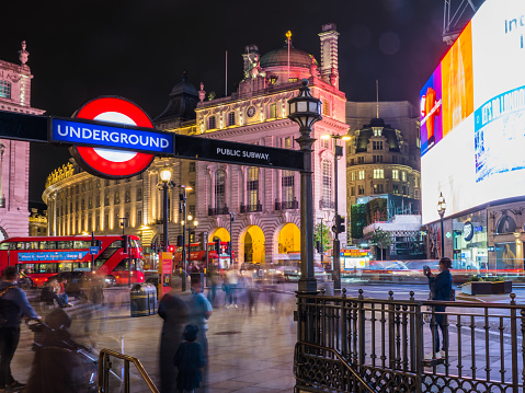 Iconic red double decker buses and the Underground sign illuminated by the neon billboards of Piccadilly Circus and Regent Street in the busy heart of London, UK.