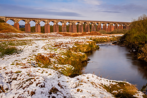 Long exposure of the Big Water of Fleet surrounded by snow in winter, with the railway viaduct in the background, Dumfries and Galloway, Scotland