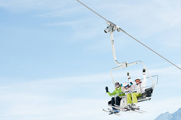Three people with arms raised up on a ski lift  stock photo