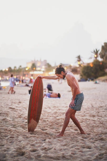 夕暮れ時にビーチでハムストリングスを伸ばすスキボーダー - skimboard ストックフォトと画像