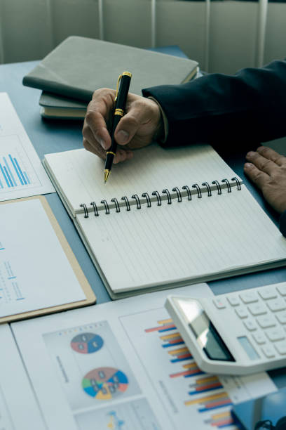 istock Young businessman analyzing business graph documents on desk with laptop computer and calculator Business and economic concepts with vertical images. 1339821184