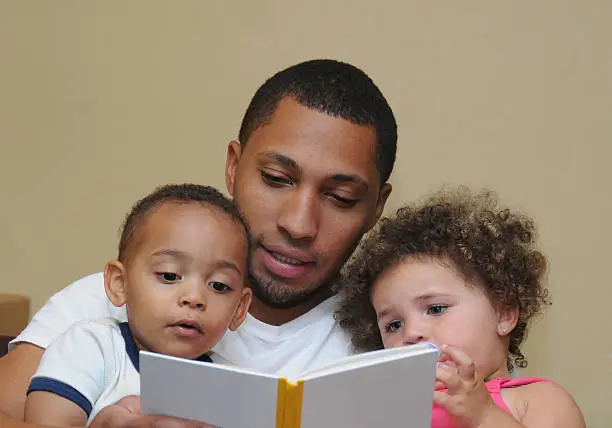 Father reading to two year old  son with dirty face and two year old niece with curly hair and blue eyes