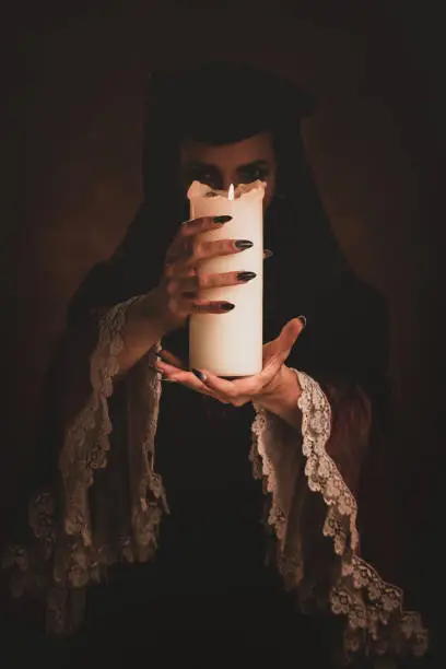 A mysterious woman in an medieval dress holds a candle.