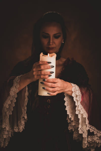Witch holding white candle casting a spell in a dark room.