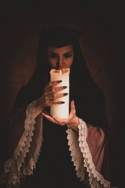 istock Witch holding white candle casting a spell in a dark room. 1339822062