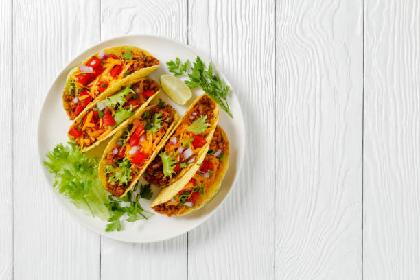 ground beef tacos with shredded cheddar cheese, fresh lettuce, tomato, onion on a white plate with lime wedges, horizontal view from above, mexican cuisine, flat lay, free space - molho verde imagens e fotografias de stock