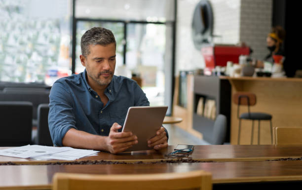 Business man working at a cafe on his tablet while waiting for a coffee