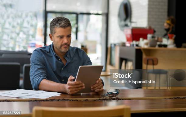 Business Man Working At A Cafe On His Tablet While Waiting For A Coffee Stock Photo - Download Image Now