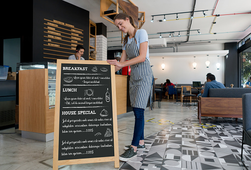 Happy waitress putting a menu board at a coffee shop and smiling - food service concepts. **DESIGN ON BOARD WAS MADE FROM SCRATCH BY US**