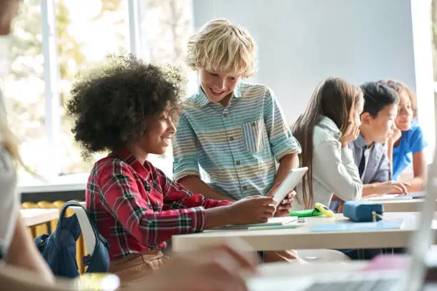 Photo of Afro American girl and Caucasian boy schoolkids working together in classroom.