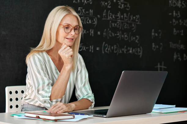 istock Happy teacher having online webinar maths lesson sitting at chalkboard. 1339829193