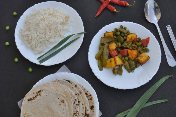 istock Rice, matar paneer mix veg and roti (Indian bread) on white plate over black background 1339830472