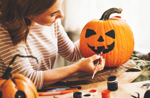 istock Young woman creating jack-o-lantern while sitting at table in kitchen at home 1339836796