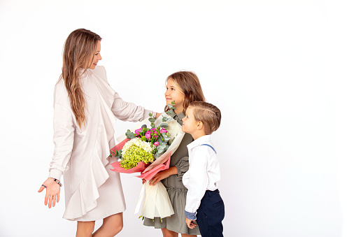 Cute boy and girl children and mother with a bouquet of flowers on a white background in the studio
