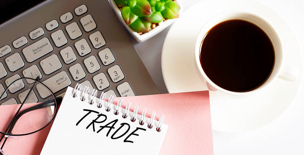 istock Office supplies, devices, coffee cup and glasses on white table with text TRADE 1339849751