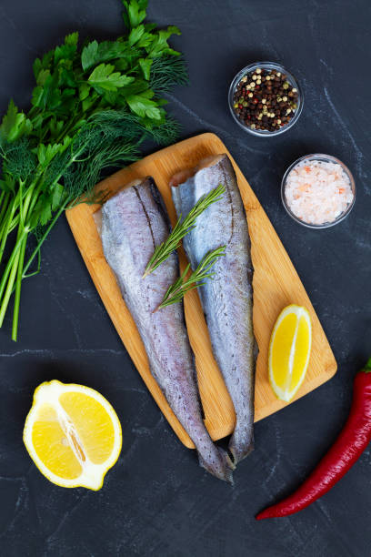 istock raw pollock fish with lemon and herbs.Uncooked pollock on wooden cutting board with ingredients for cooking on black stone table. fresh seafood with lemon, salt and pepper. Top view with copy space. 1339852088