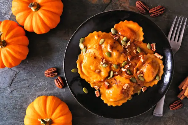Pumpkin filled ravioli pasta with nuts and pumpkin seeds. Table scene, above view on a dark background.