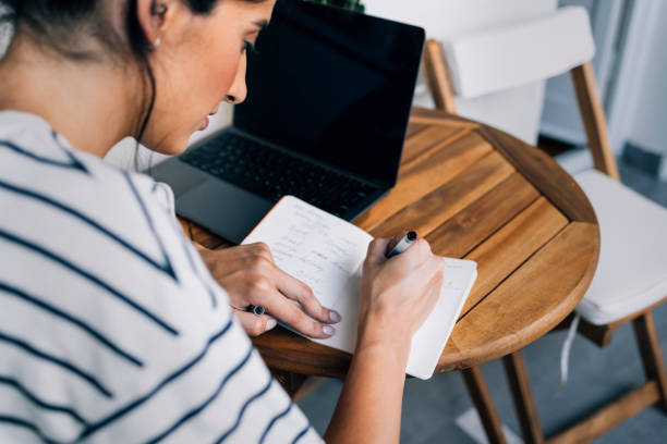 istock Anonymous Woman Sitting at a Wooden Table, Using her Laptop and Taking Notes 1339854945