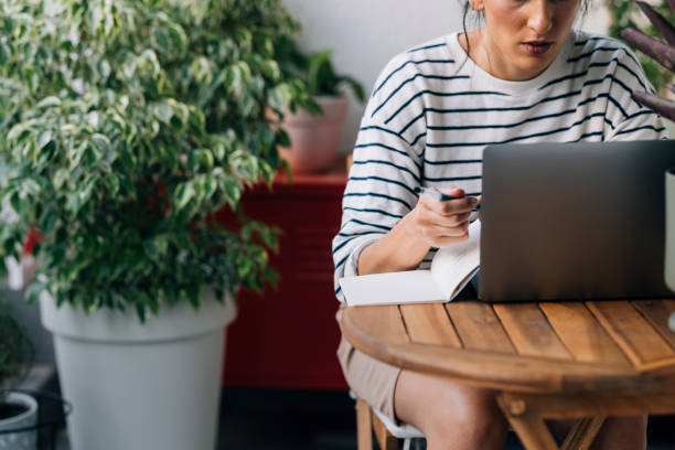 istock Anonymous Woman Sitting at a Wooden Table, Using her Laptop and Taking Notes 1339854949