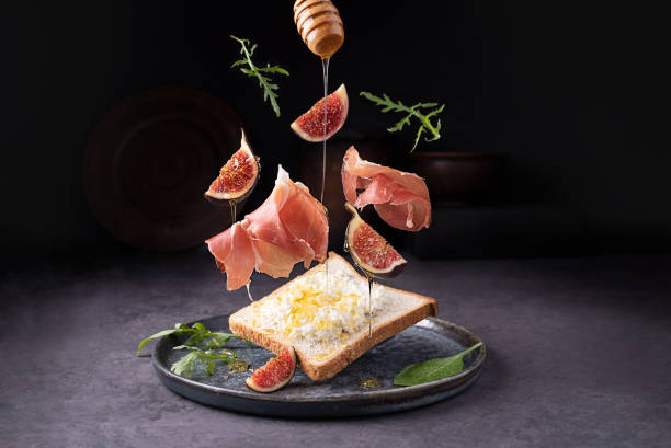 crostini with prosciutto ricotta and figs, flying italian ham and fruit on a dark background, toast with jamon. - crostini imagens e fotografias de stock