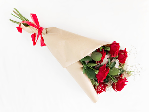 Red roses wrapped in brown kraft paper and tied with a red ribbon on a white background