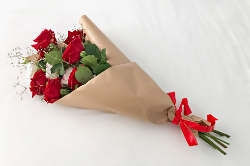 Red roses wrapped in brown kraft paper and tied with a red ribbon on a white background