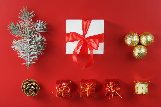istock White box with padark and red bow around Christmas decorations with spruce branches on a red background 1339866117